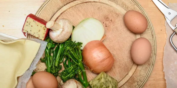 A wooden cutting board with eggs, vegetables, and cheese, ready for cooking.