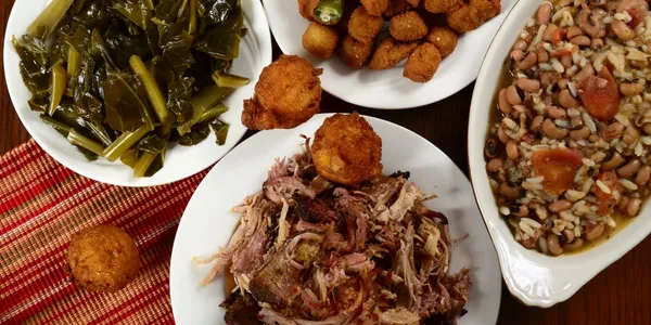 A Southern meal featuring pulled pork, collard greens, fried okra, cornbread, and a bean and rice dish.